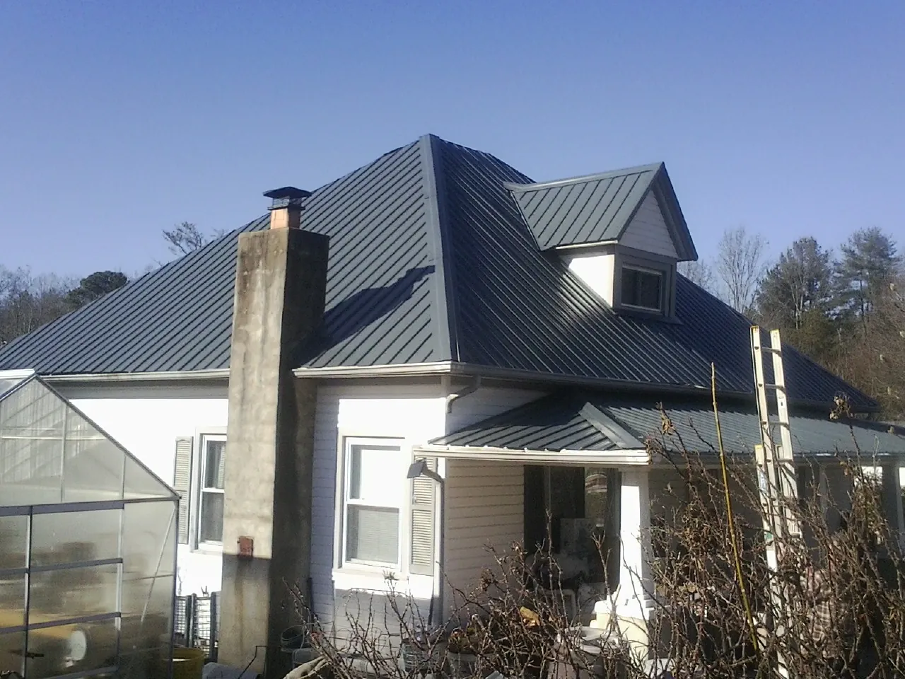 Dark blue standing seam metal roof on a white farmhouse with dormer — Slate & Tile Roof Repair by Roofing Brothers in Leominster