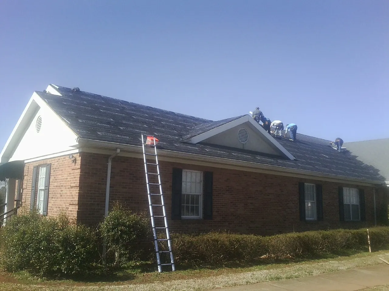 Crew tearing shingles off a brick ranch roof with a ladder set — Metal Roof Repair work by our crew in Leominster