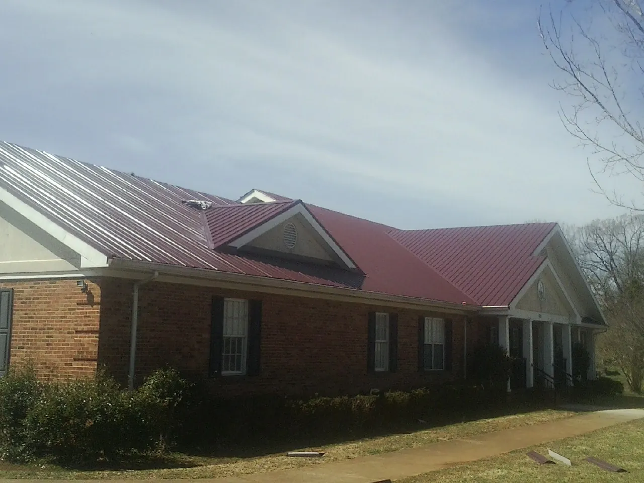 Red metal roof with gabled entries on a long brick building, from a Hail Damage Roof Repair job in Leominster