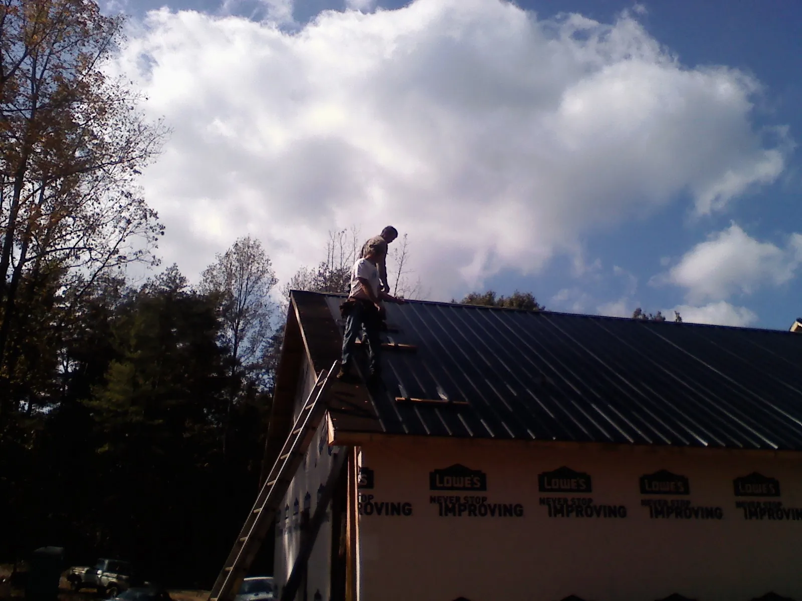 Roofer fastening dark metal panels high against a cloudy sky, from a Roof Inspection job in Leominster