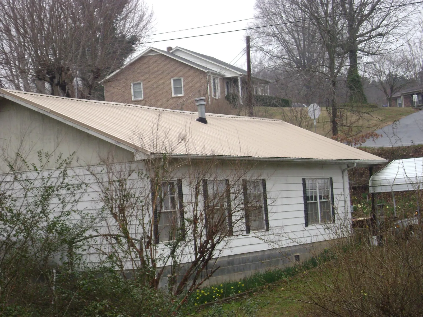Tan metal roof on a white sided house set into a hillside — Commercial Roofing by Roofing Brothers in Leominster